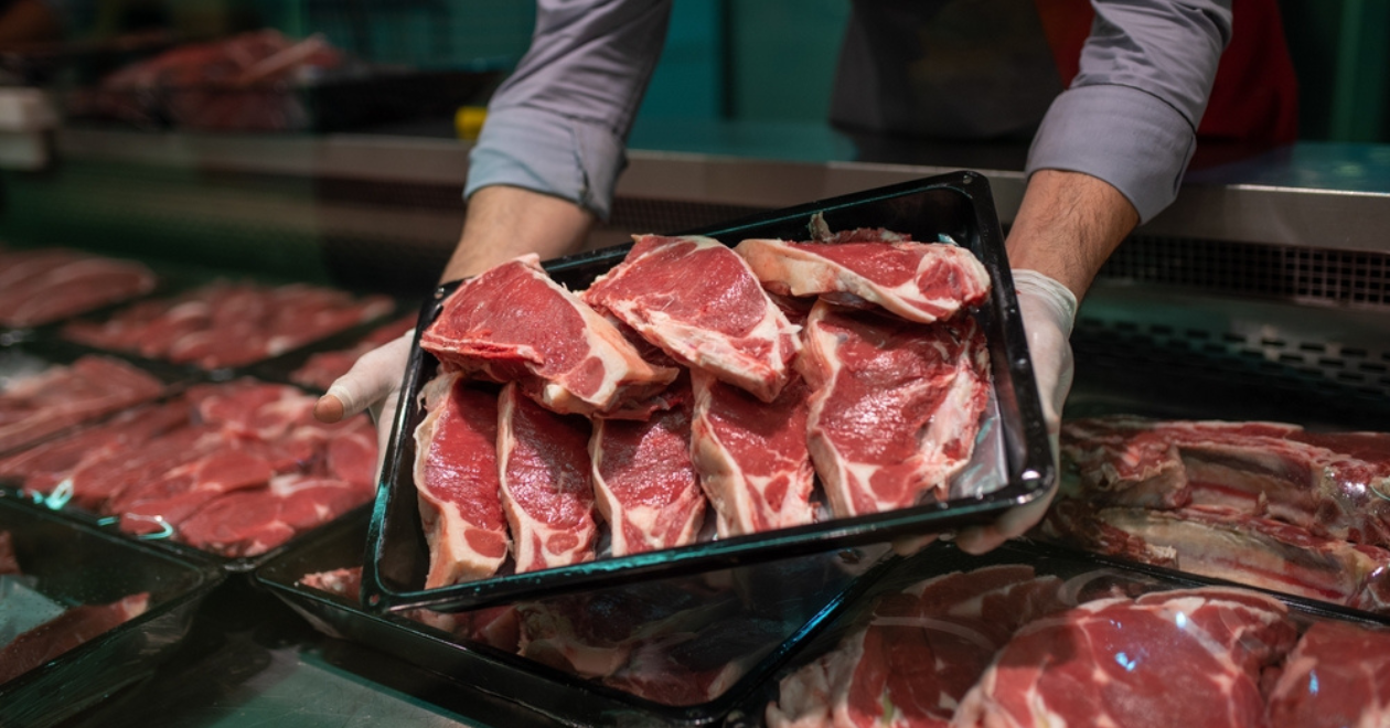 Person holding pack of meat over meat counter