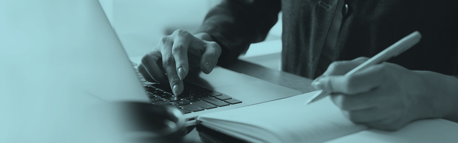 Person doing online training on a laptop and writing notes on a pad