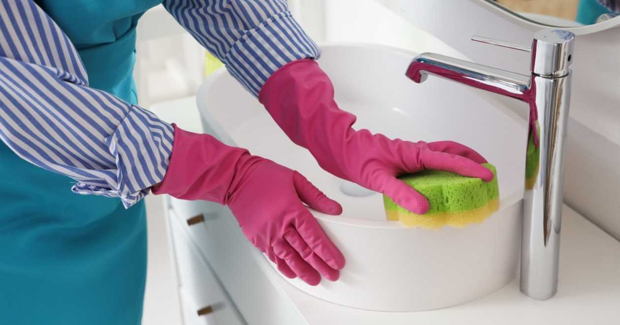 Person with rubber gloves cleaning bathroom sink