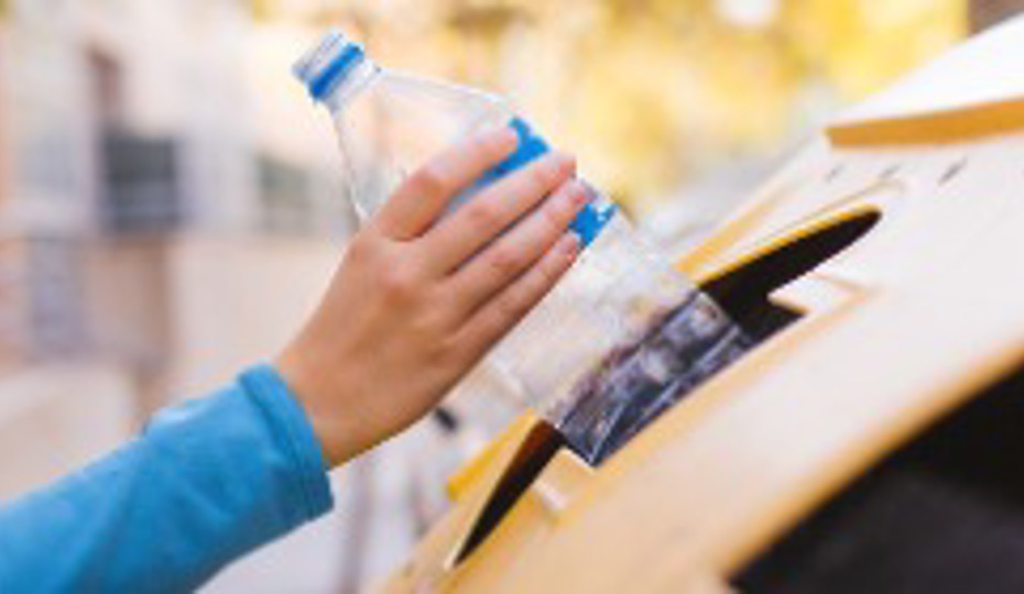 Hand recycling a plastic bottle in a yellow container