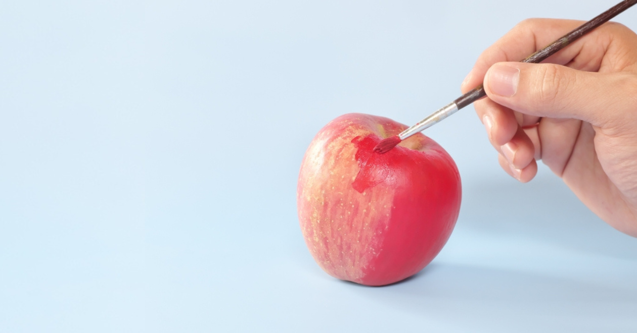 Hand painting an apple with artificial red colorant or paint - fraudulent food concept