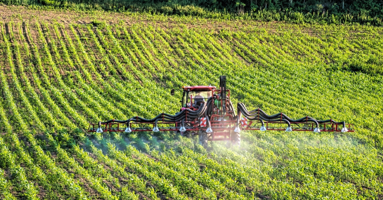 Farm tractor spraying pesticides over a field 