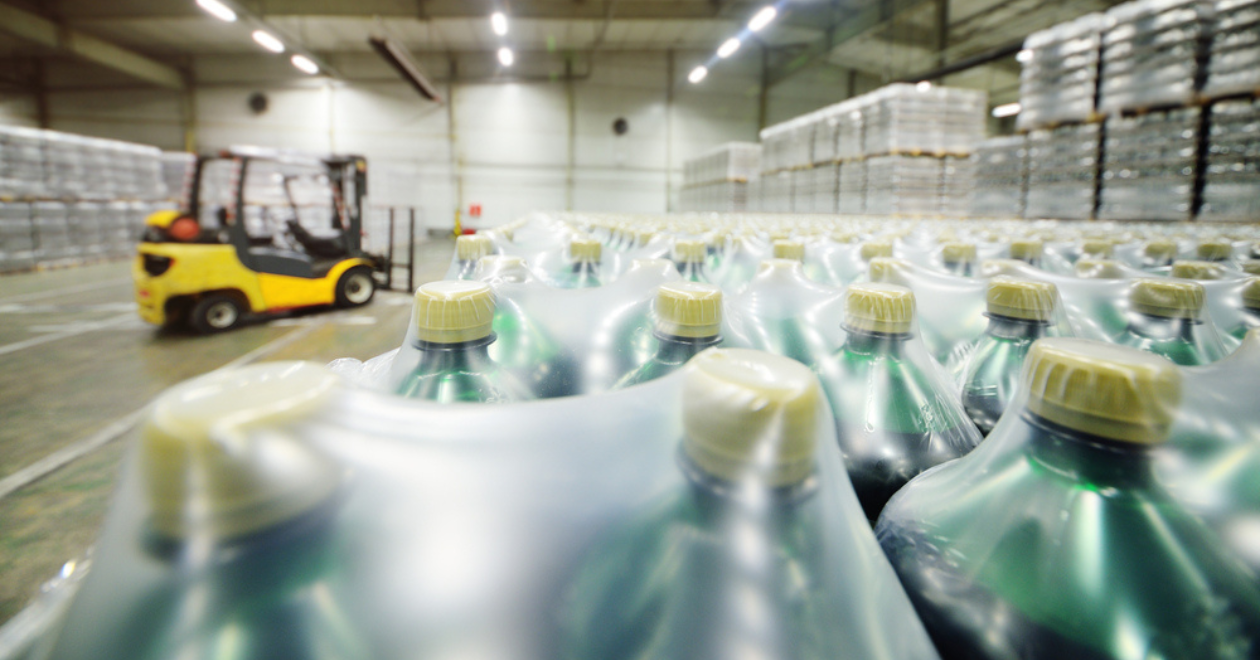 Yellow loader on the background of a huge industrial food warehouse with plastic PET bottles with beer, water, drinks.