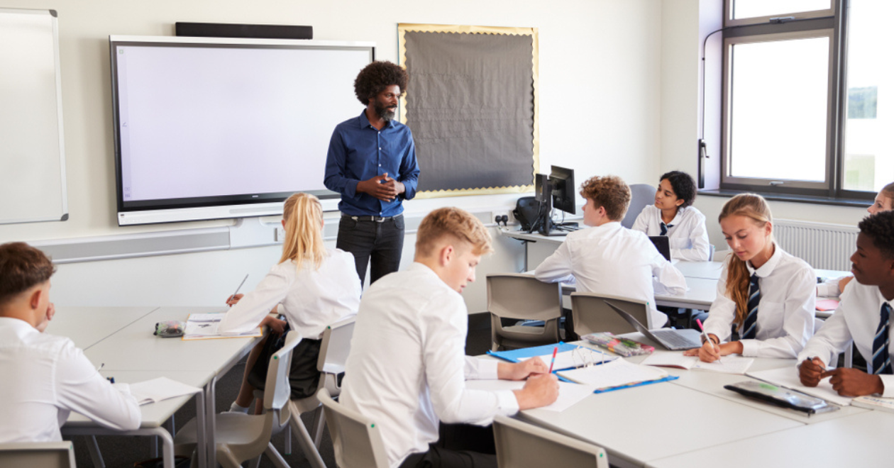 Teacher standing next to interactive whiteboard and teaching lesson to pupils